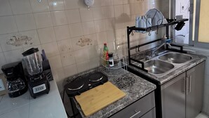Una cocina con encimera de granito, estufa, pileta y escurreplatos.