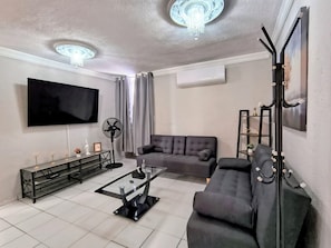A living room with a flat-screen TV, a sofa, a coffee table, and a floor lamp. - Modern Apartment with 100% Air Conditioning • King-Size Beds (Ciudad Lázaro Cárdenas)