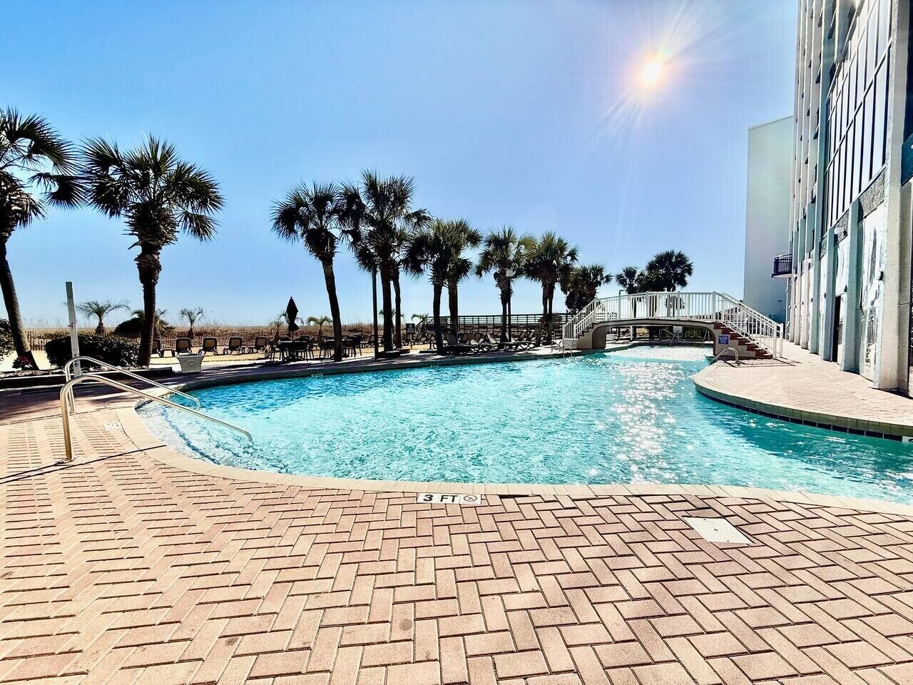A swimming pool with palm trees, a brick deck, and a building with columns.