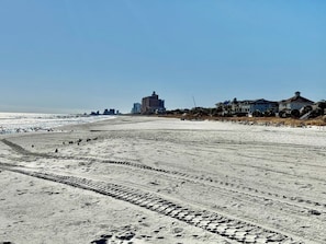 Ein Strand mit Fußabdrücken, einem klaren Himmel und Gebäuden in der Ferne.