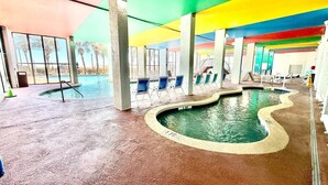 An indoor swimming pool with a wavy edge, surrounded by lounge chairs and concrete pillars.