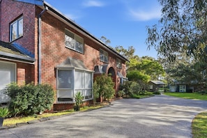 A residential house with a brick facade, large windows, and a driveway leading to a street. - Ling House Retreat - Oasis on 13th Beach Golf Course (Connewarre)