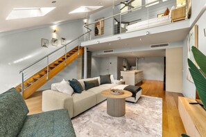 Un vaste espace de vie comprenant un grand canapé, une table basse et un escalier menant à un niveau supérieur.