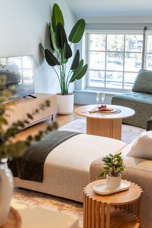 A modern living room with a large window, a sofa, a coffee table, and a potted plant. - Spacious Waterfront Loft at Woolloomooloo Wharf (Woolloomooloo)