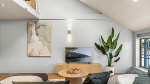 A modern living room with a sofa, a coffee table, a television, a large plant, and artwork on the wall. - Spacious Waterfront Loft at Woolloomooloo Wharf (Woolloomooloo)
