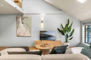 Ein modernes Wohnzimmer mit einer Couch, einem Couchtisch, einem Fernseher, einer großen Pflanze und Kunstwerken an der Wand.
