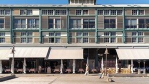 A multi-story building with a flat roof, large windows, and a covered outdoor seating area with tables and umbrellas. - Spacious Waterfront Loft at Woolloomooloo Wharf (Woolloomooloo)