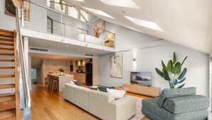 A modern loft apartment with a mezzanine, open-plan living area, kitchen, and a large window providing natural light. - Spacious Waterfront Loft at Woolloomooloo Wharf (Woolloomooloo)