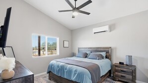 Une chambre à coucher avec un lit, une table de chevet, un téléviseur, un ventilateur de plafond et une fenêtre.