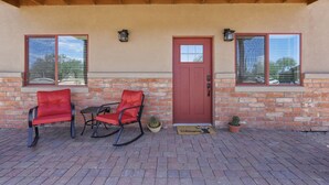 Une terrasse couverte avec deux fauteuils à bascule, une porte rouge et un mur en briques.
