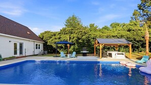 Ein Garten mit Schwimmbad, überdachter Grillgelegenheit und Gartenmöbeln.