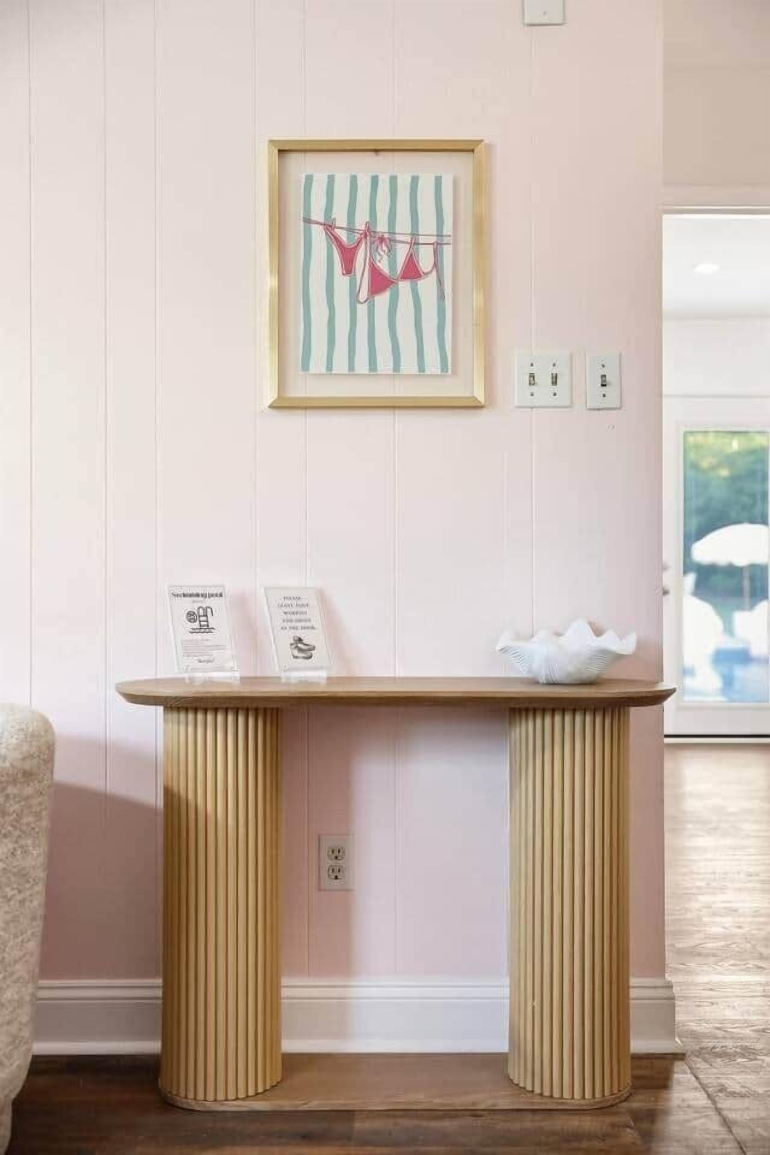 A room with a wooden table, a framed artwork, and a small white basket.