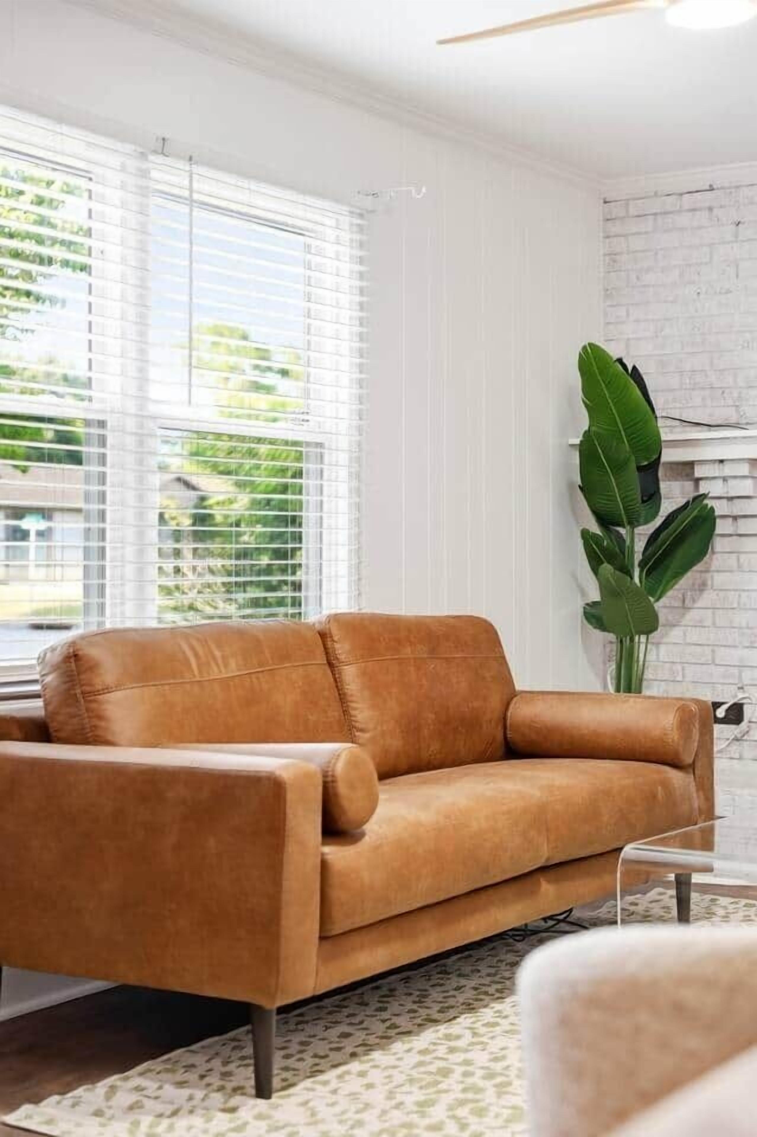 A modern living room with a leather sofa, a white brick wall, and a large green plant.