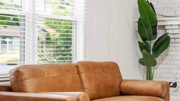 A modern living room with a leather sofa, a white brick wall, and a large green plant.