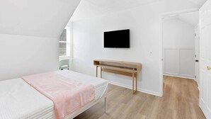 Ein Schlafzimmer mit einem Bett, einer hölzernen Bank, einem Deckenventilator, einem an der Wand befestigten Fernseher und einer Tür zu einem weiteren Raum.
