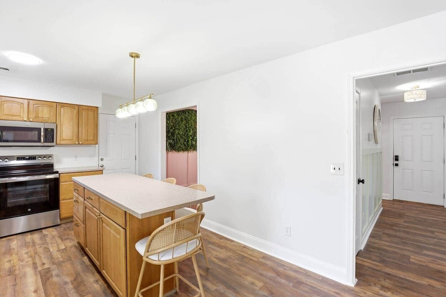 A kitchen with wooden cabinets, a built-in microwave, a stainless steel oven, a light-colored countertop, a bar stool, and a hanging light fixture.