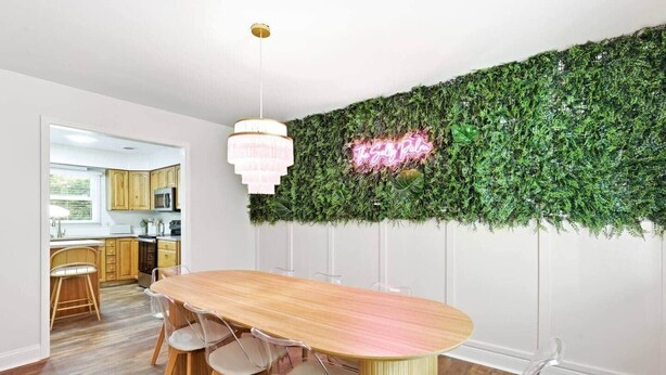 Ein Essbereich mit einem Holztisch und -stühlen, einer hängenden Leuchte und einer Wand mit einer begrünten Wand und einem Neonlichtschild.