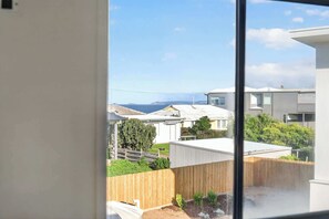 Blick aus einem Fenster auf ein Wohngebiet mit Holzzaun, Garten und Häusern, bewölkter Himmel und Land in der Ferne.
