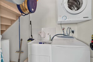 Un lavadero con lavadora de carga frontal, un lavabo y una manguera.