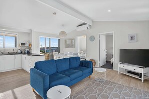 Un salon moderne avec un canapé bleu, un téléviseur et un coin repas offrant une vue agréable.