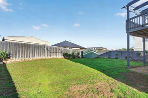 Une cour arrière clôturée avec une pelouse, une terrasse en bois et une structure métallique.