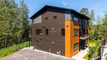 A modern two-story building with a flat roof, large windows, and a mix of brown and orange exterior panels.