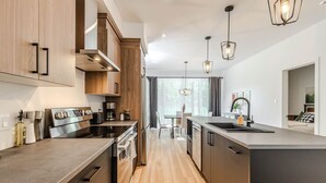 Une cuisine moderne dotée d’un îlot central, d’appareils électroménagers en acier inoxydable et de luminaires suspendus.