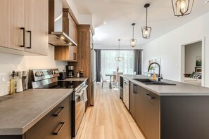 Een moderne keuken met een centraal kookeiland, roestvrijstalen apparatuur en hanglampen.