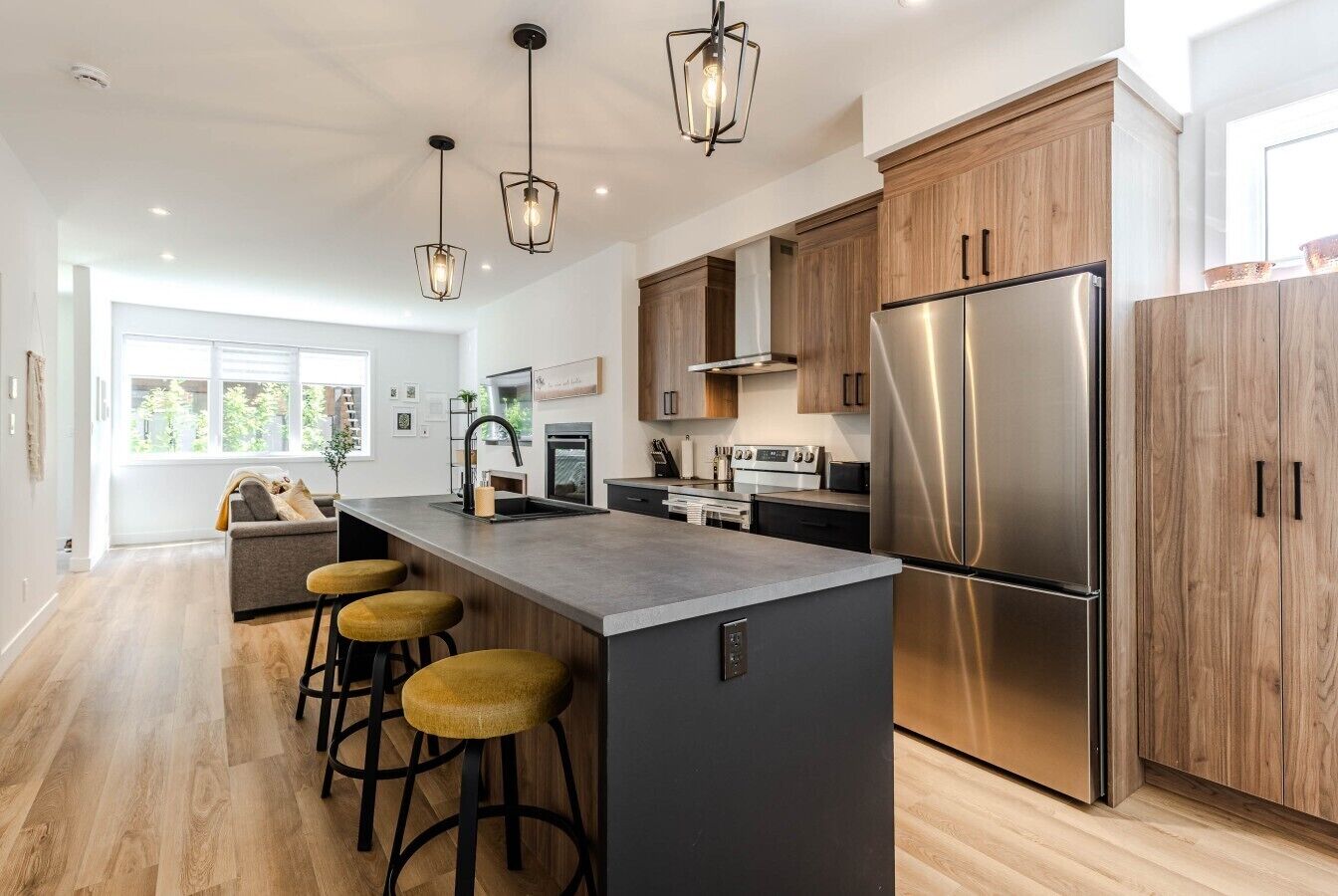 A modern kitchen with a central island, bar stools, stainless steel appliances, and wooden cabinetry.