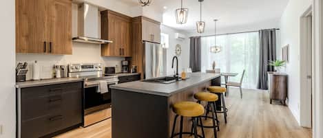 A modern kitchen with wooden cabinets, a central island with stools, and pendant lighting.