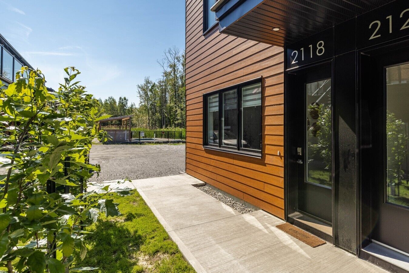 Un bâtiment moderne avec une façade en bois, une entrée numérotée et une allée gravillonnée.