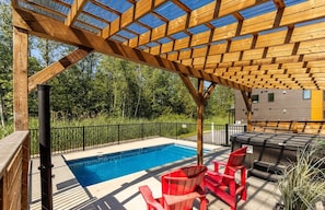 Una terraza de madera con piscina, sillas rojas y una pérgola.