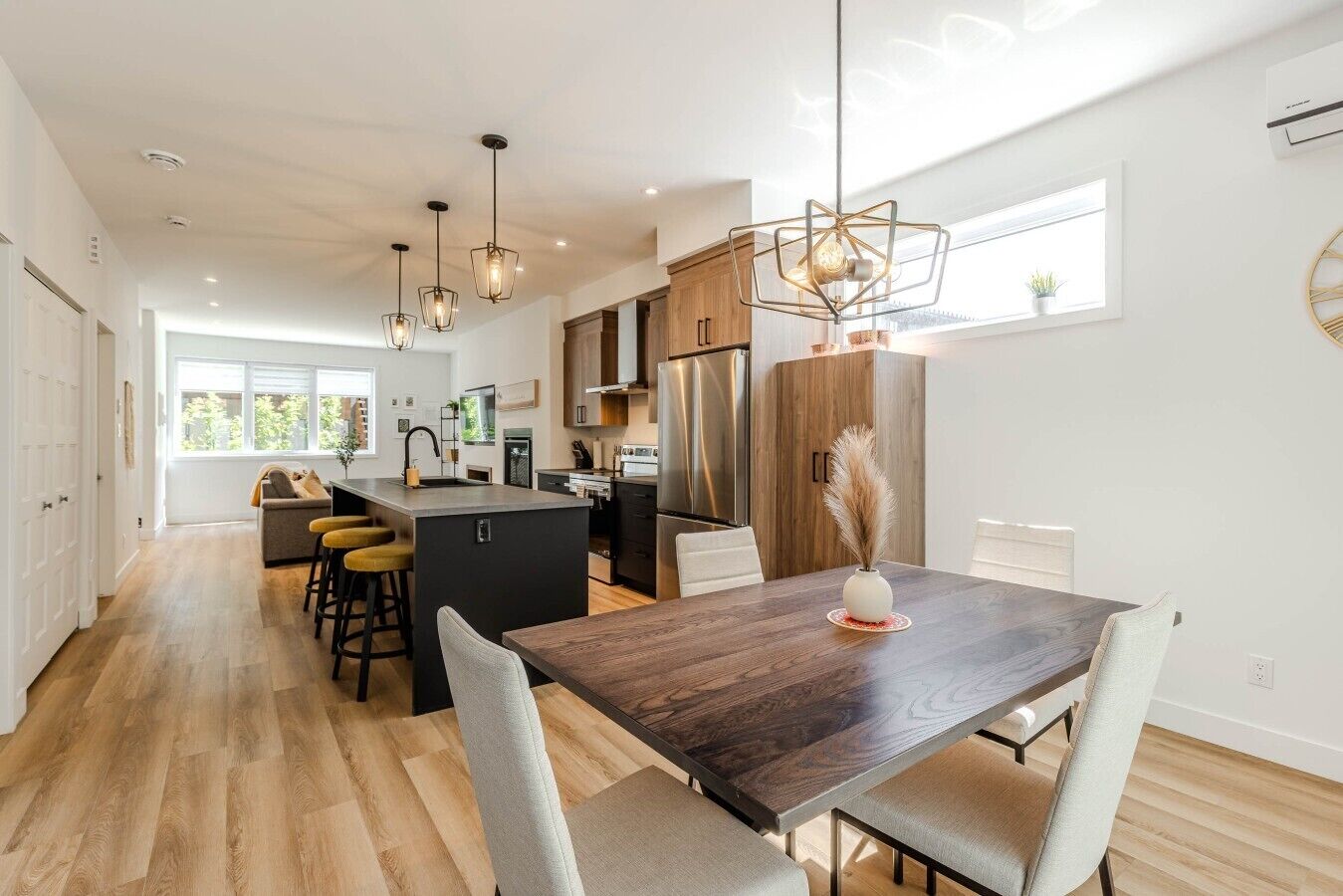 A modern kitchen with a central island, pendant lighting, and a dining area with a wooden table and chairs.