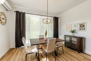 Un comedor con una mesa de madera, cuatro sillas, una lámpara de araña, un aparador y un reloj en la pared.