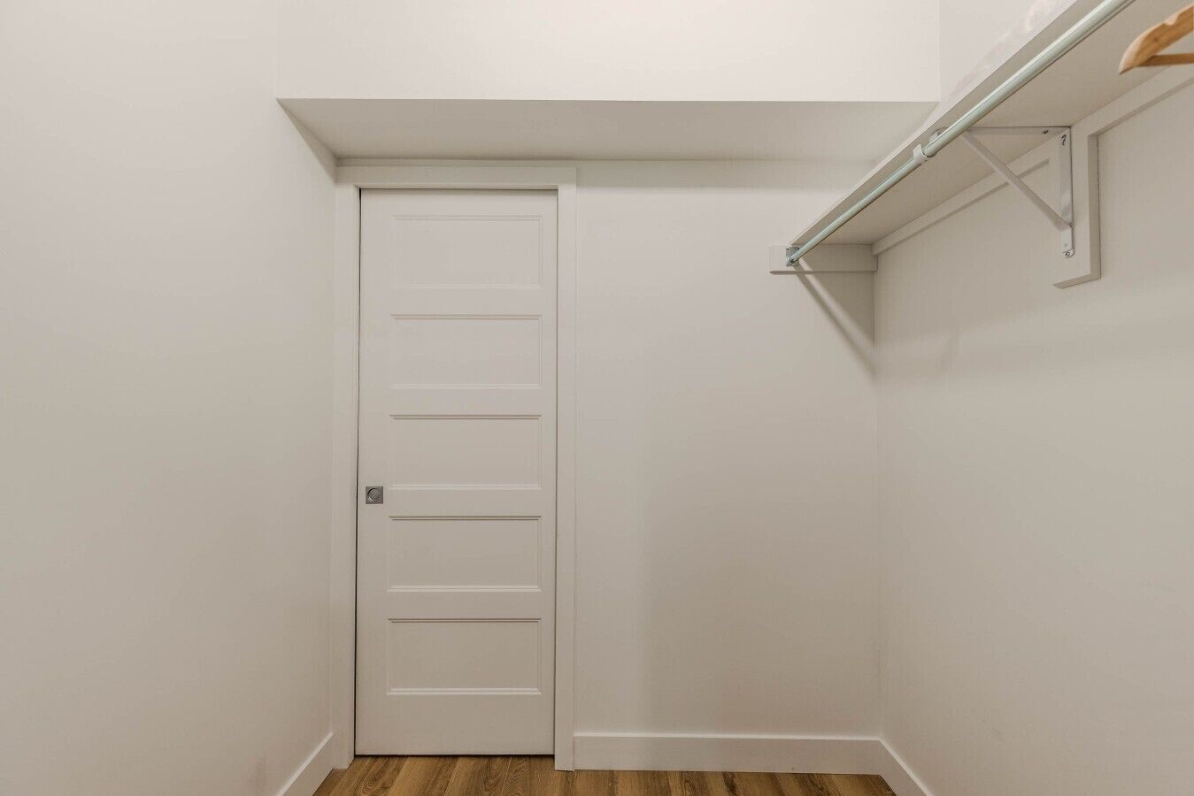 Una puerta blanca de diseño sencillo, suelo de madera y un accesorio metálico en la pared.