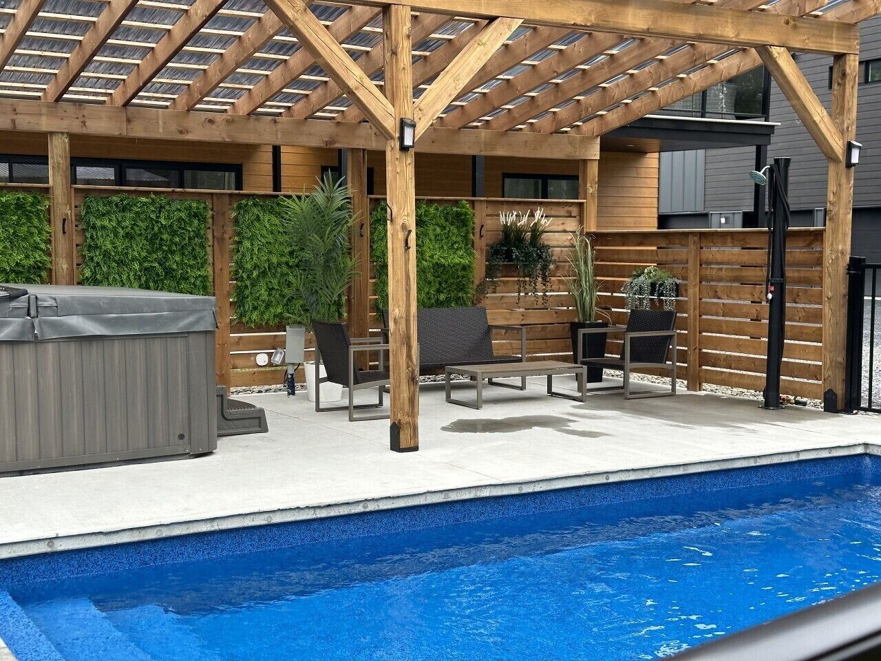 A covered outdoor area with a pool, wooden pergola, lounge chairs, and a hot tub.