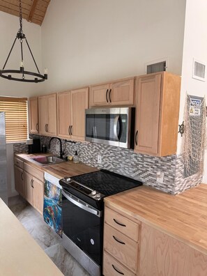A kitchen with wooden cabinets, a stainless steel microwave, a dishwasher, and a black stove. - Heart of the Key Cottage (Marathon)