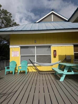 A yellow building with a covered deck, two turquoise Adirondack chairs, a hammock, and a picnic table. - Heart of the Key Cottage (Marathon)