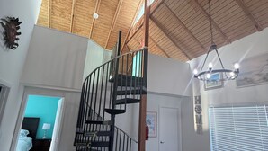 A spacious living area with a high ceiling, a wooden staircase, a sofa, a coffee table, and a view of the outside. - Heart of the Key Cottage (Marathon)