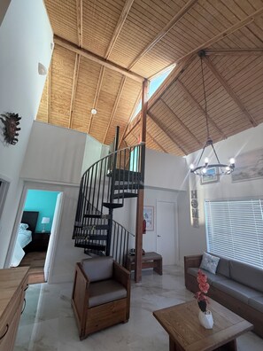 A spacious living area with a high ceiling, a wooden staircase, a sofa, a coffee table, and a view of the outside. - Heart of the Key Cottage (Marathon)