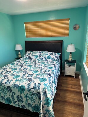 A bedroom with a bed, two bedside tables, a clock, and a window with blinds. - Heart of the Key Cottage (Marathon)