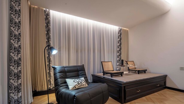 A modern living room with a leather sofa, a side table, a lamp, and a large window with curtains.