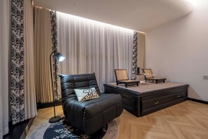 Uma sala de estar moderna com um sofá de couro, uma mesa lateral, uma luminária e uma janela grande com cortinas.