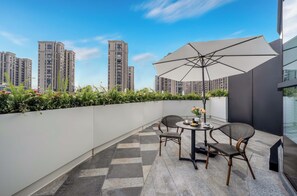 Terraço no telhado com mesa, cadeiras, guarda-sol e vista para edifícios altos.