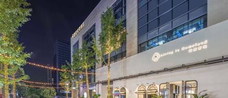 A modern hotel with a glass facade, outdoor seating, and string lights.
