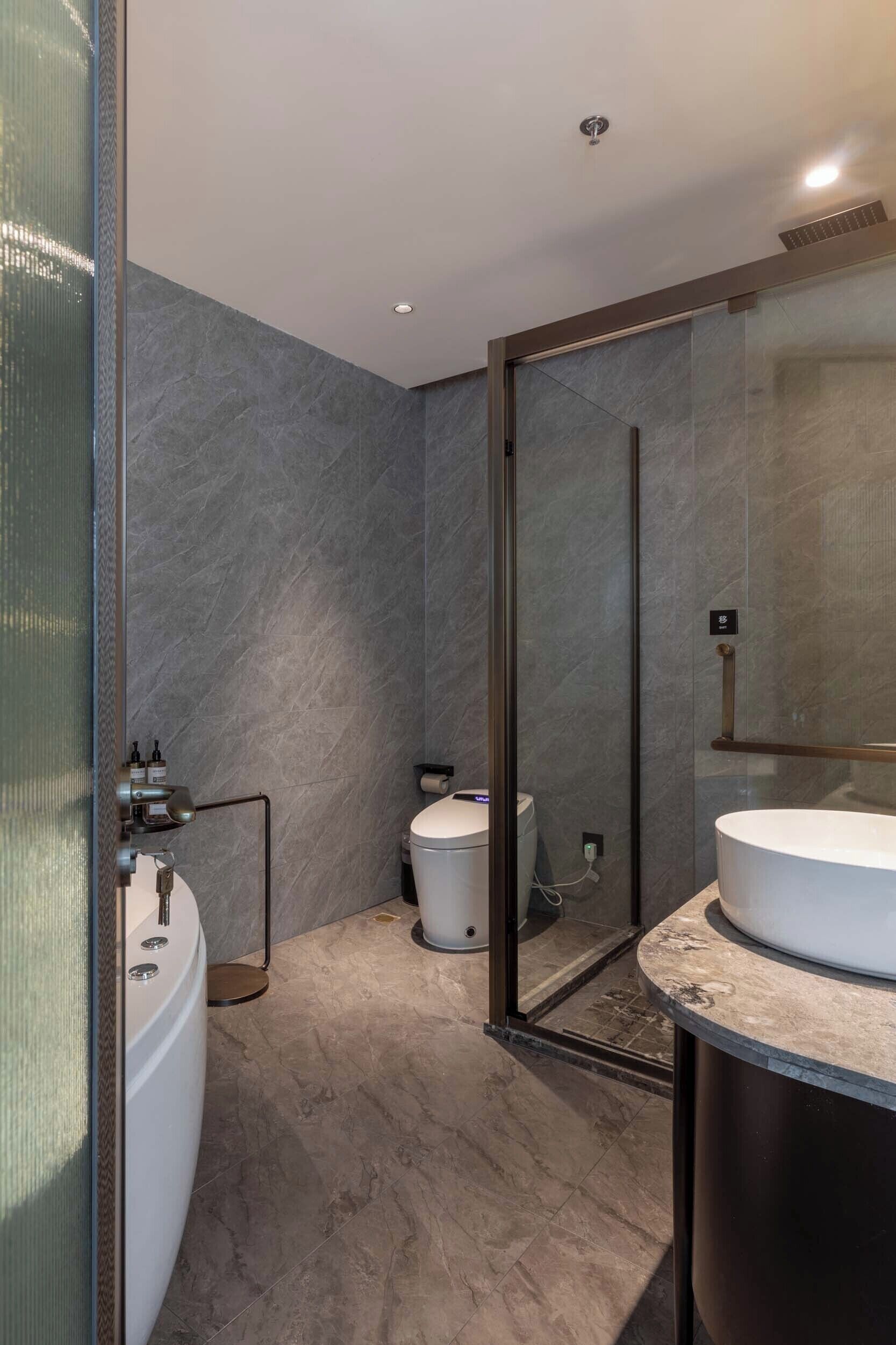 A modern bathroom with a glass-enclosed shower, a standalone toilet, and a vanity with a large mirror.