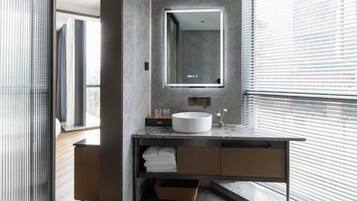 A modern bathroom with a marble countertop, a round sink, a mirror, and a window with blinds.