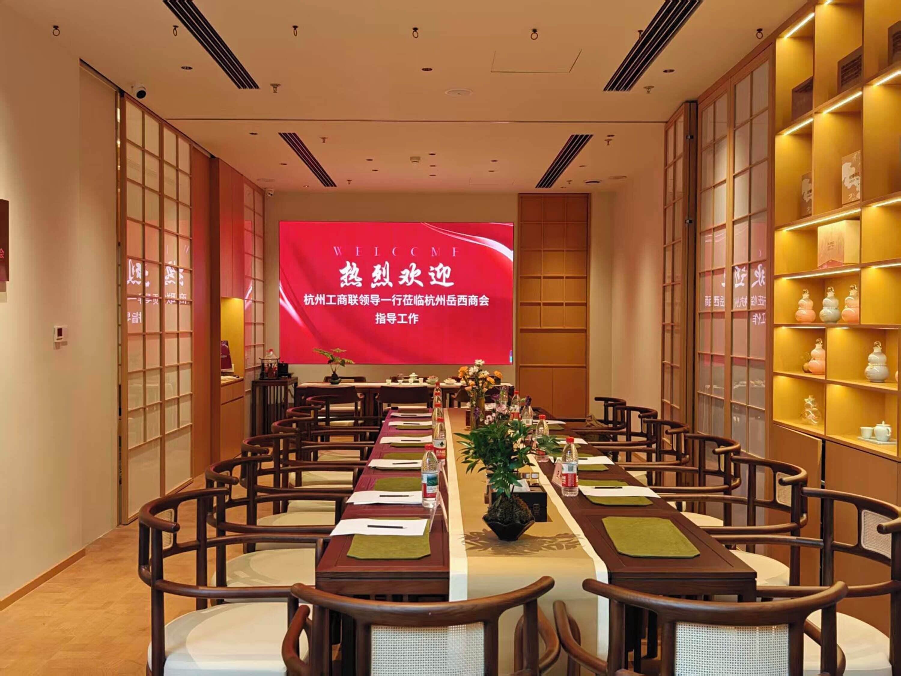 A conference room with a long table, chairs, a large screen, and shelves with decorative items.
