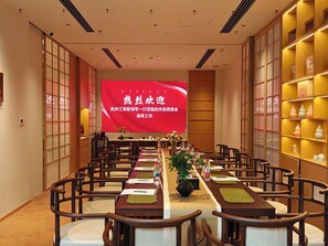 Un salón de conferencias con una larga mesa, sillas, una pantalla grande y estanterías con elementos decorativos.
