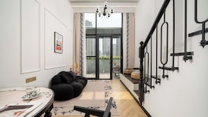 A modern living room with a black sofa, a dining table with a cup and saucer, and a chandelier.